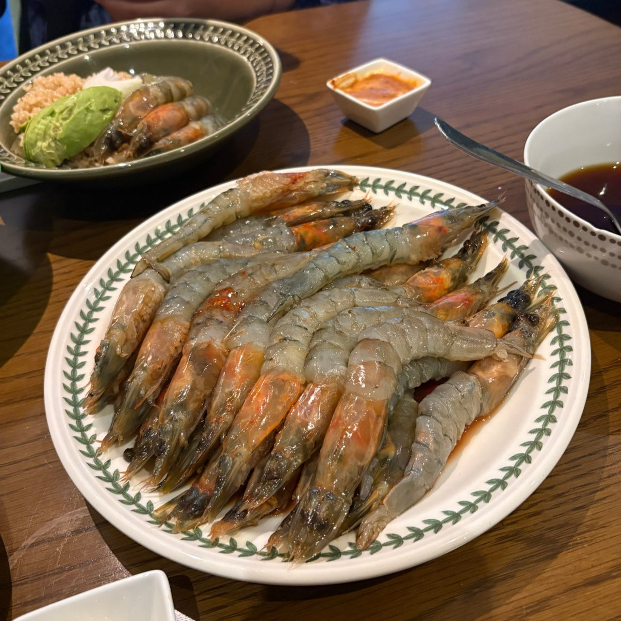 Platter of cooked shrimp on a wooden table with side dishes.
